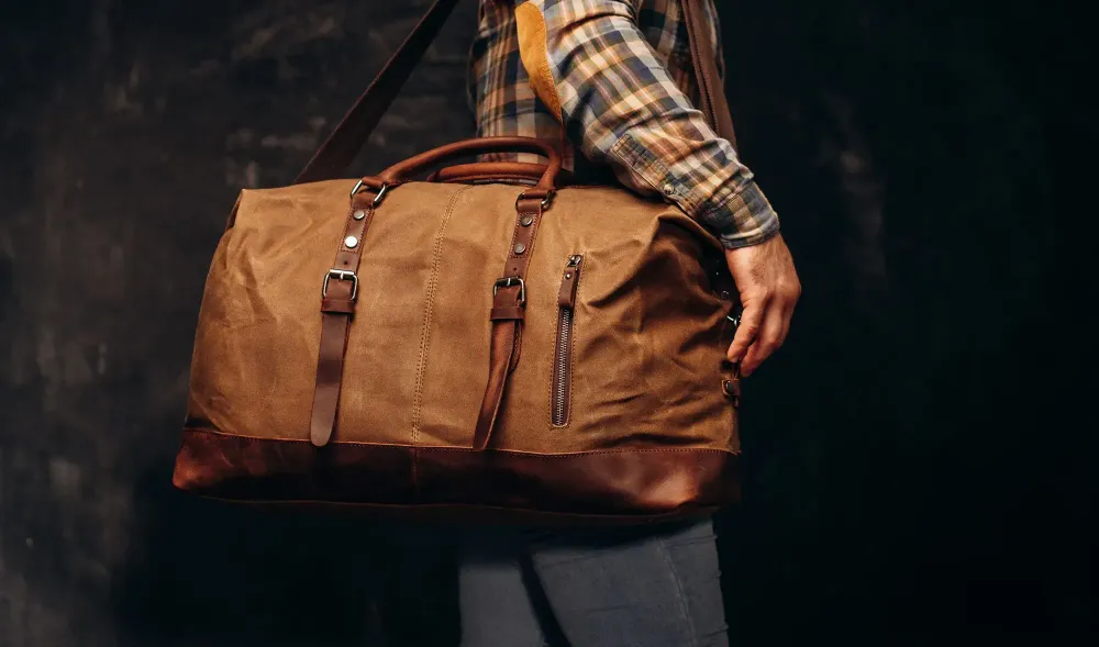 Close up of man holding a brown leather duffel bag